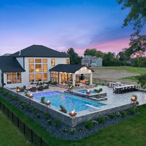 A pool with the works! This gunite swimming pool is surrounded by a spacious travertine patio. The pool includes color changing lighting, a sun ledge, bench seating and laminars. See more: <https://www.pool-fx.com/recent-projects/outdoor-living-at-its-best-westerville-oh> #swimmingpool #gunitepool #outdoorliving Gradual Pool Entry, Big Decks Backyard, Pools Landscaping Ideas, Inground Pools With Hot Tubs, Square Pool With Waterfall, Inground Pool Layout Ideas, Outside Patio Ideas With Pool, Backyard Decor With Pool, Outdoor Living Pool Area