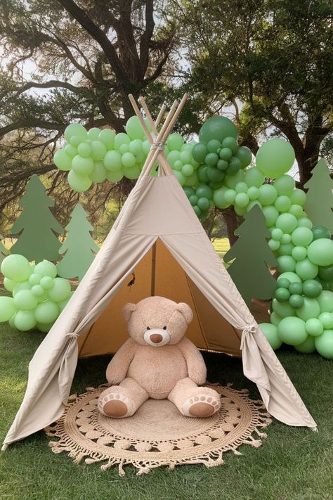 One Happy Camper first birthday party setup featuring a beige teepee with a large teddy bear sitting inside. The backdrop includes green balloon garlands and tree cutouts, creating a perfect outdoor themed photo spot for a camping-themed 1st birthday celebration. One Happy Camper First Birthday Diy, One Happy Camper First Birthday Games, Camper Smash Cake, Happy Camper Smash Cake, One Happy Camper First Birthday Girl, One Happy Camper Smash Cake, Birthday Creative Ideas, Camping First Birthday, Camper Decorations