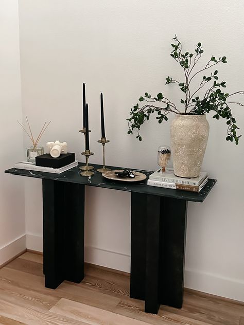 Entryway Console table decor Console Table : Burke Decor Vase : Pottery Barn Plant stems: Amazon Camera Candle : Gift from @kelir from CB2 Diffuser: Pottery Barn Black Candles: Amazon Candle Stand : Gift from @anniemescall Coffee Table Books : Amazon #homedecor #home #entrywaydecor #consoletable #homestyle Hallway Stand Entry Tables, Vase On Entryway Table, Black Console Decor, Walkway Table Decor, Small Black Entryway Table, Black Console Table Styling, Console Table Hallway Luxury, Black Coffee Table Styling, Black Entry Table Decor