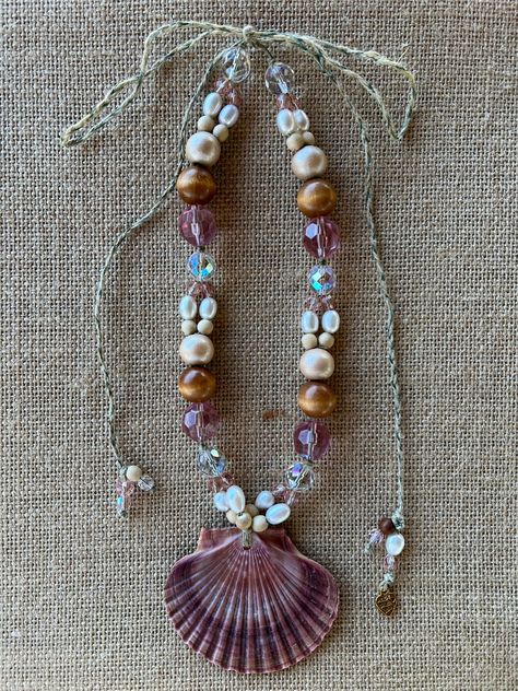 Mexican flat shell pink necklace. Handmade one of a kind. Clear, pink, fresh water pearl and wood beads. Roman gold coin inside shell. Adjustable tie to compliment any neckline and garment. Jingle Shell Jewelry, Shell And Bead Necklace, Pink Handmade Necklace, Sea Themed Necklace, Handmade Shell Jewelry, Sea Shells Necklace, Handmade Shell Necklace, Diy Seashell Necklace, Beaded Jewelry Photography