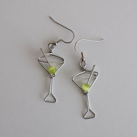 Martini Glass Earrings. Great gift for Bartenders, Hostesses and Waitresses. NOW AVAILABLE IN TWO SIZES. Regular martini glass is 1 1/2 inches high, small martini glass is 1 1/8 inches high (not including earring hooks, see inset photo for scale). Tiny wire martini glasses, complete with green cat's eye bead.  Surgical steel hooks are hypo-allergenic. Clear plastic stoppers on backs. Aluminum wire will not tarnish. I have been making custom wire art and jewelry for 30 years. I started in 1989 se Martini Wire Earrings, Wire Wine Charms, Stud Wire Earrings, Wire Earring Designs, Wire Earring Ideas, Unique Diy Earrings Ideas, Wire Earrings Diy, Selfmade Earrings, Wire Jewelry Ideas