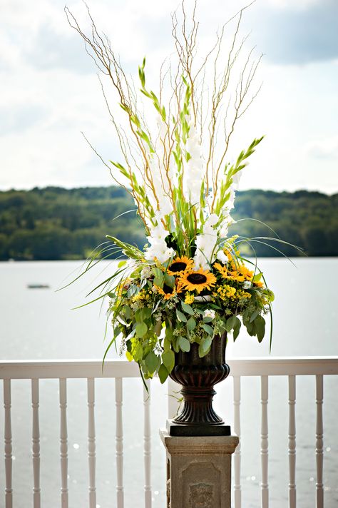 large urn filled with sunflowers and gladiolus and grass for the lakeside ceremony Tall Sunflower Arrangements, Sunflower Altar Arrangement, Large Sunflower Arrangements, Gladiolus Arrangements Vase, Gladiolus Flower Arrangements Vase Wedding Centerpieces, Green And Yellow Floral Arrangements, Sunflower Urn Arrangement, Lakeside Ceremony, Gladiolus Arrangements