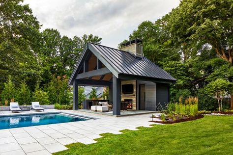 The stone patio of this modern backyard has uneven edges to create visual interest in this modern space. The sleek metal roof is a dark contrast to the custom chimney and fireplace. Pool Pavilion Ideas, Pool House Cabana, Lap Pool Designs, Pool House Design, Backyard Pool Design, Pool Pavilion, Poolside Dining, Pool Remodel, Pool Cabana