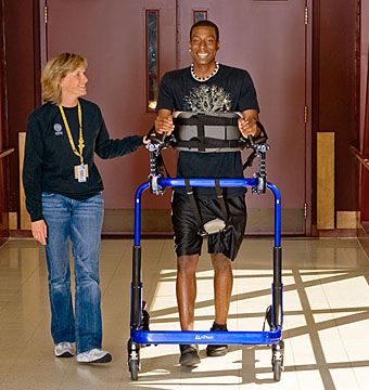 A young man works in rehabilitation on overground gait training in the Rifton Pacer gait trainer. Gait Trainer, Gait Training, Treadmill, Stationary Bike, Train