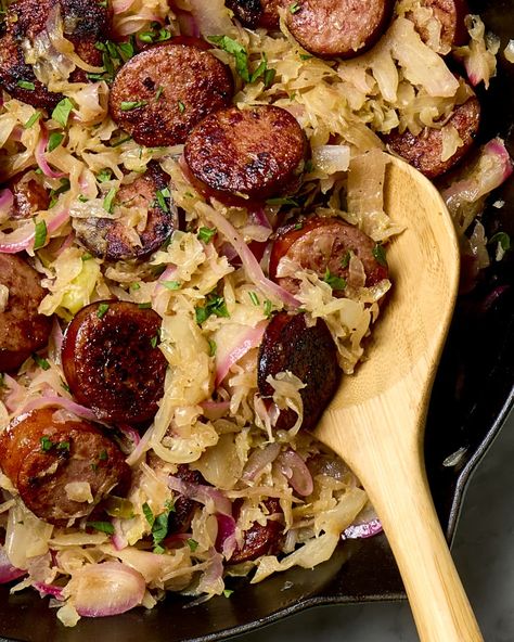 close up shot of cooked sauerkraut and sausage in a cast iron pan, with a wooden spoon resting in the bottom right part of the pan. Sausage And Kraut, Sausage And Sauerkraut, Sauerkraut Recipe, Parsley Leaves, Homemade Sauerkraut, Kielbasa Sausage, Sauerkraut Recipes, One Pan Dinner, Kielbasa