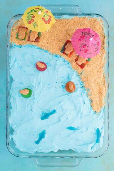 This beach theme poke cake would be a hit at a beach theme party or under the sea theme party! Kids will have fun decorating the top of this beach cake with teddy grahams, gummy sea creatures, and graham cracker sand. #beachpokecake #pokecake #beachcake Diy Beach Cake Birthday, Third Birthday Beach Theme, Beachy Birthday Cake Ideas, Diy Ocean Cake, Easy Beach Theme Cake, Simple Ocean Theme Cake, Beach Theam Birthday Party, Easy Beach Cake, Beach Theme Sheet Cake