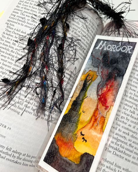 2.5” x 7” bookmark depicting scene of Mordor from Lord of the Rings - a fiery mountainous area with an active volcano painted in orange and black colors. Laminated in clear plastic, 10 mil thick. A black tassel is tied and looped through the plastic. Lotr Bookmark Diy, Colored Pencil Bookmarks, Paint A Bookmark, Lord Of The Rings Diy Gifts, Lord Of The Rings Gift Ideas, Watercolor Art Bookmarks, Lotr Bookmark, Lord Of The Rings Watercolor, Lord Of The Rings Bookmark