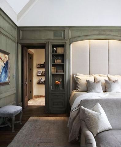 Master bedroom with green stained wood paneling and built-in shelving surround an oversized upholstered headboard, at the foot of the bed is a grey sofa with matching accent pillow, the room has dark wood flooring and a large neutral area rug Closet Behind Bed, Tudor Design, Headboard From Old Door, Modern Tudor, Bed Nook, Tudor Revival, Bookcase Headboard, Headboard Designs, Bed In Closet