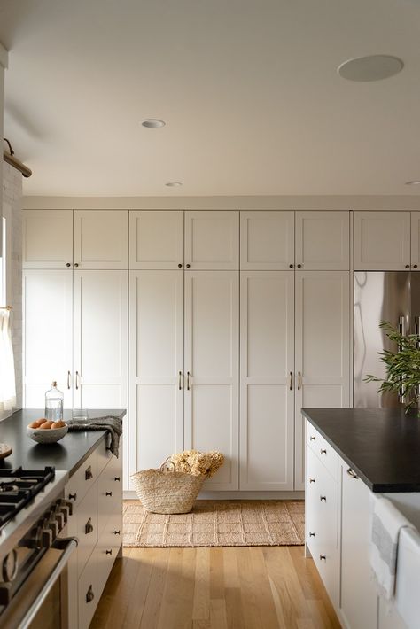 Modern farmhouse kitchen featuring old world charm and European influences. This kitchen has ceiling to counter handmade ceramic backsplash tiles paired with a patina soapstone counters. Warm tones layered in with unlacquered brass accents in the light fixtures and cabinetry hardware. Painted greige cabinetry seamlessly integrate with the contrast trim throughout the home. Featuring floor to ceiling built-ins to provide extra functionality for the growing family.