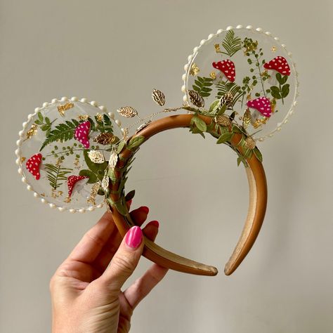 For all the Cottagecore girlies! These resin mouse ears are unique and fun, with an earthy vibe and a touch of glam, perfect for any fairy princess 🍄🧚. A neutral headband is accented with a gold leaf crown and vines, and the mushrooms and greenery stand out in clear, shiny resin, sparkly with flecks of gold and finished with pearl trim. A perfect complement to your theme park outfit, these whimsical ears are lightweight and absolute show stoppers. Our mouse ears are intended for women and adul Princess Disney Ears, Creative Mickey Ears, Unique Mickey Ears, Custom Disney Ears, Aesthetic Mickey Ears, Cute Disney Ears, Disney Ears Diy, Resin Mickey Ears, Cottagecore Mouse