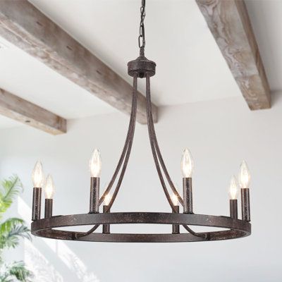 This rustic chandelier farmhouse presents a wagon wheel silhouette with 8 candle-style lamp holders perched atop in matte black and imitation wood grain, which cleverly reflect a sense of industrial farmhouse style. Finish: Antique Distressed Black | Farmhouse Chandelier 8 Lights Black, Gracie Oaks Wagon Wheel Chandelier, Dining Room Lights Fixture, Rustic Foyer Chandeliers | 19.6 H x 23.6 W x 23.6 D in | Wayfair Round Candelabra Chandelier, Rustic Dining Chandelier, Front Entry Light Fixture Modern, Chandelier Farmhouse Dining, Farmhouse Dining Table Lighting, Modern Country Light Fixtures, Dining Room Lighting Over Table Rustic, Mountain House Lighting, Chandelier Dining Room Round