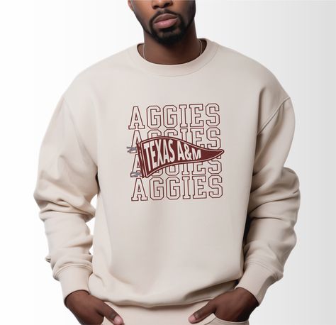 A model wears the Sand Adult Unisex Texas A&M Aggies Pennant Crewneck Sweatshirt.  The ﻿Texas A&M Aggies Pennant﻿ graphic is in bold Black in a Varsity style. Vintage College Apparel, College Merch Ideas, Spiritwear Designs, College Shirt Ideas, Collegiate Design, Collegiate Apparel, Spirit Wear Designs, School Spirit Shirts Designs, Aggie Pride