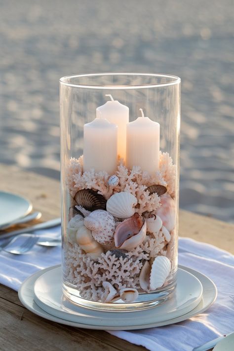 Beach-themed wedding centerpiece with seashells and candles layered in a glass vase, perfect for a coastal wedding. Beachy Centerpieces, Beach Wedding Centerpieces Diy, Beach Wedding Table Settings, Nautical Wedding Centerpieces, Beach Theme Wedding Reception, Coastal Wedding Centerpieces, Beach Theme Centerpieces, Affordable Wedding Centerpieces, Ocean Wedding Theme