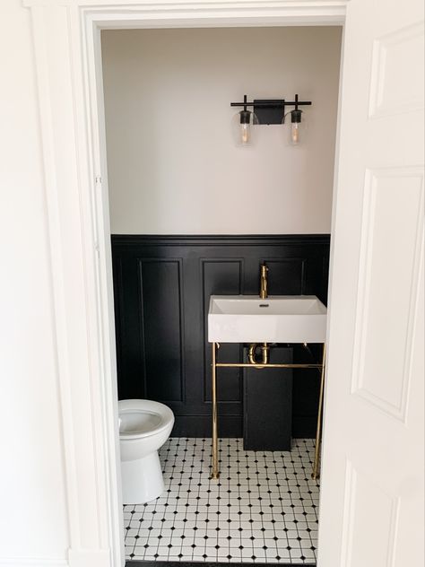 This photo is of a half bathroom with black wainscoting half way up the wall, a gold pedestal sink and black and white penny tile on the floor. Bathroom Black Wainscoting, Gold Pedestal Sink, Black Wainscoting Powder Room, Penny Tile Bathroom Black And White, Black Panelled Bathroom, Black Wanescoting Bathroom, Pedestal Sink Bathroom Ideas Modern, Black Panel Bathroom, Bathroom Remodel With Pedestal Sink