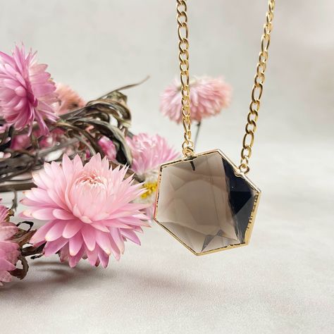 Embrace the allure of nature's beauty with our exquisite Smoky Quartz Hexagon Necklace 💎. This unique piece features a stunning Smoky Quartz stone, expertly cut into a captivating hexagon shape and plated with luxurious gold on the edges. The stone gracefully hangs from a high-quality stainless steel Figaro chain, allowing you to choose the perfect chain length to suit your style. Key Features:     Hexagon Elegance: The Smoky Quartz stone takes center stage, cut into a mesmerizing hexagon shape that measures approximately 1.5 inches. Its distinct shape and rich color make it a true statement piece.     Gold-Plated Accent: The edges of the Smoky Quartz stone are meticulously plated with gold, adding a touch of opulence and sophistication.     Stainless Steel Chain: The necklace is complete Hexagon Necklace, Crystal Necklaces, Figaro Chain, Hexagon Shape, Center Stage, Quartz Stone, Smoky Quartz, Stainless Steel Chain, Nature Beauty