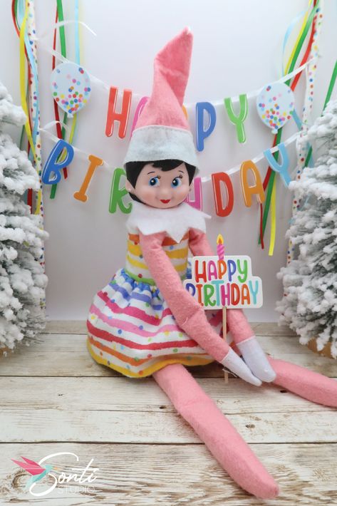 Elf wearing a two-piece rainbow colored dress holding a "Happy Birthday" sign in front of a mini happy birthday banner Elf On The Shelf Birthday Party, Elf On Shelf Birthday, Elf Birthday Ideas, Birthday Elf On The Shelf Ideas, Elf On The Shelf Birthday Visit, Elf On The Shelf Birthday Ideas, Elf Birthday Party, Elf On The Shelf Birthday, Elf Birthday