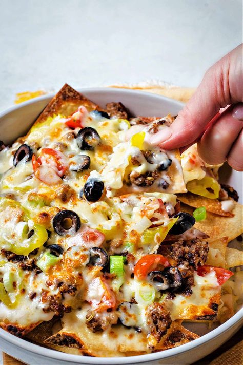 a hand picking up an Italian nacho from the pan. Zios Italian Nachos Recipe, Johnny Carinos Italian Nachos Recipe, Italian Nachos Old Chicago, Different Types Of Nachos, Meatball Nachos, Stuffed Nachos, Italian Nachos Recipe, Football Brunch, Chilli Nachos