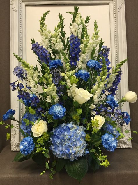 A stunning alter piece created to the tune of a blue and white color schemed wedding. Debuting blue hydrangea, white roses, white snap dragons, blue carnations, and blue delphinium #blueandwhite #alterarrangement #weddingflowers Shades Of Blue Flower Arrangements, Hydrangea And Delphinium Centerpiece, Blue Hydrangea And White Roses Flower Arrangements, Large Blue Floral Arrangements, Blue Purple And White Flower Arrangements, Royal Blue Floral Arrangements, Blue Hydrangea Arrangements, Blue And White Floral Arrangements, Snap Dragons