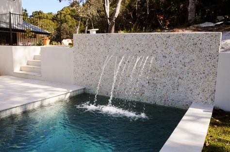 A stone and mortar wall at the edge of one pool with several fountains streaming from the horizontal crack and into the narrow, long pool.