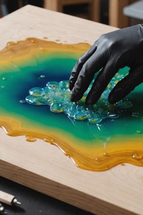 Hand in a black glove touching a colorful resin art piece with green, blue, and orange swirls on a wooden surface. How To Paint With Resin, How To Polish Resin Epoxy, Resin Marble Effect, Resin Pour Art, Mixed Media Resin Art, Resin Ocean Art, Diy Resin Mold, Amazing Resin, Fume Hood