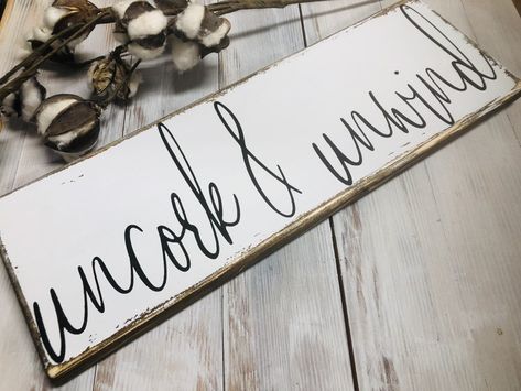 "Uncork and unwind wood sign. This distressed farmhouse sign will make a great addition to your kitchen dining room or wine bar. Description Size: 5.5 x 16\" (pictured) and variations available Background is done in white chalk paint Lettering is done in black chalk paint Hanging hardware is attached and ready to be hung Sign has been hand painted and distressed for a rustic farmhouse look Your sign may slightly differ due to the natural characteristics of wood ie grain, knots and divots." Home Wine Bar, Wine Bar Sign, Farm House Dining Room, Farmhouse Kitchen Signs, Home Bar Signs, Built In Wine Rack, Black Chalk Paint, Coffee Bar Signs, Farmhouse Style Sign