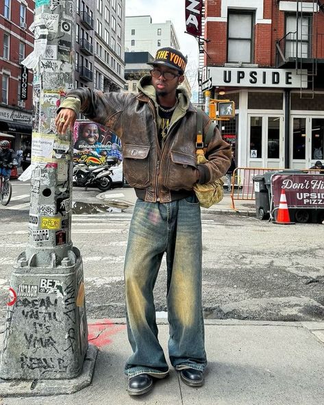 Vintage Vibe 🍩 How about his color? 📸 @knawtkai 🇺🇸 🧢Cap : free the youth 👔Hoodie : trendtvision 👞Shoes : dr.martens 👜Bag : louis vuitton Embodying the vintage vibes of American streets, this man’s outfit exudes timeless coolness. The combination of the vintage brown leather jacket and washed baggy jeans sets the tone, while the ‘Trendtvision’ khaki zipped hoodie and black printed shirt add depth to the ensemble. Elevating the look further, the ‘Dr. Martens’ black boots and ‘Free the Y... Brown Jacket Men Outfit, Baggy Jeans With Boots, Black Leather Jacket Outfit Men, Brown Leather Jacket Outfit Men, Brown Boots Outfit Men, Dr Martens Outfit Men, Converse Men Outfit, Insta Recreate, Dr Martens Bag