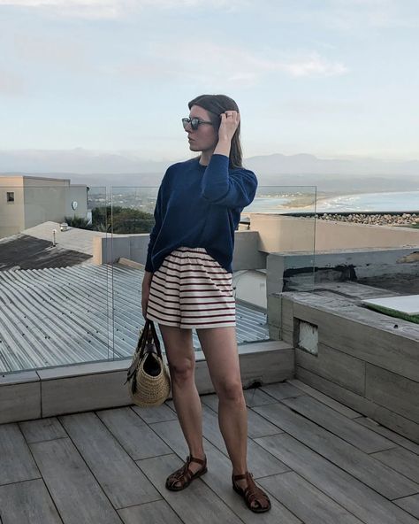 A woman stand on a balcony. She wears red and white striped shorts, brown fisherman sandals, a blue jumper and a basket bag Jumper Shorts, Flight Outfit, Blue Jumper, Fisherman Sandals, Summer Vacation Outfits, Summer Shorts Outfits, Summer Outfit Inspiration, Summer Shorts, Striped Shorts