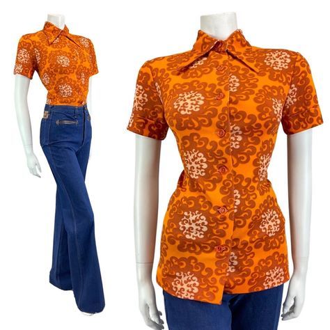 This is a bold vintage blouse made from a mid-weight, knitted polyester fabric with a good amount of stretch and no additional lining. Featuring a sharp dagger collar, orange button fastenings down the centre front, darts in the bust and body for a flattering shape, and short fitted sleeves. Covering the fabric is a beautiful repeating swirled pattern in shades of orange. This gorgeous blouse is designed to be worn a little more fitted to the body which will be reflected in the recommended size, and would look great paired with a vintage skirt or pinafore dress - so check out our other items to complete your perfect outfit. This blouse would best fit: 10 (12 due to the stretch of the fabric) please check your measurements against the ones provided below, Bust: 36" Sleeve (pit to cuff): 3" 70s Button Up Shirt Outfit, 70’s Clothes, 60s Clothing, 70s T Shirts, 70s Orange, Uniform Ideas, 70s Blouse, Fashion Decades, 60s Women