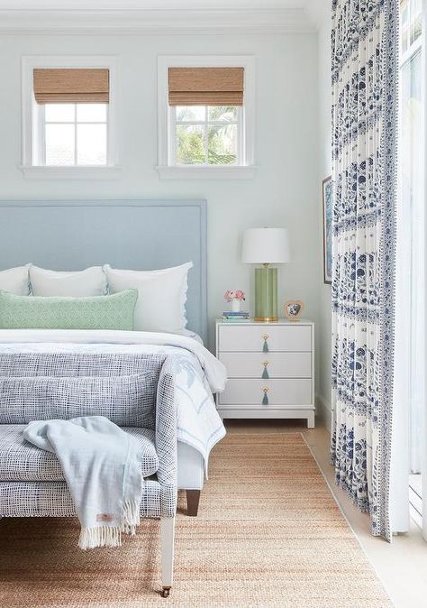 Small windows covered in bamboo roman shades and framed by a pale blue wall are located above a light blue headboard accenting a bed covered in white and blue bedding topped with a green lumbar pillow layered in front of white and blue shams. White And Blue Bedding, Blue Dorm Room Ideas, Blue Dorm Room, Kalamkari Border, Blue Green Bedrooms, Blue Dorm, Interiors Bedroom, Blue Headboard, Light Blue Walls