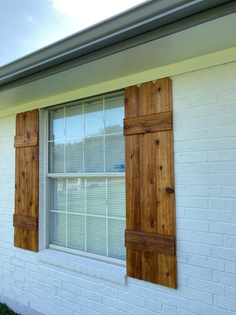 DIY shutters, made with cedar fence pickets, and hellmans clear sealer. Cedar Wood Shutters, Cedar Board And Batten Shutters, Wooden Outdoor Window Shutters, Farmhouse Wooden Shutters, White Brick House Cedar Shutters, White Brick House With Cedar Shutters, Cedar Shutters On Brick House, Barnwood Shutters Exterior, Rustic Wooden Shutters Exterior