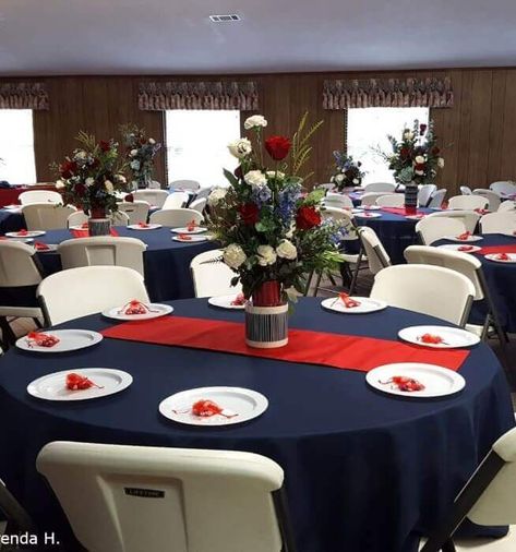 Set a dazzling tablescape by incorporating a classic red and blue color combination into your décor. Drape the table with a navy blue tablecloth and spread a red table runner on top for a fascinating allure. Exquisitely arrange white & red roses along with foliage in a unique vase to impart a majestic charm. Place white plates along with red rose stems to exude an enthralling appeal elevating your event decor to the next level. Patriotic Table Decor, Runner Wedding Table, Blue Graduation Party, Satin Table Runner, Pipe And Drape Backdrop, Red Wedding Decorations, Wedding Table Runner, Table Runner Wedding, Blue Tablecloth