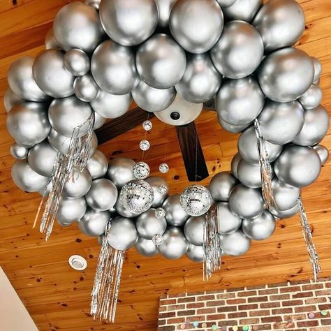 Nothing screams more extravagant than sparkly chandeliers and you can take that to the next level with balloons. Using metallic chrome silver latex balloons, form a round base and build more layers until you get the size you want. Add more character to your decor by hanging silver foil tassels and strings of silver disco balls. Wow your guests with a sparkle of balloon chandelier that's truly one for the books. Disco Ball Balloon Ceiling, Balloon Arch Disco Ball, Disco Balls Hanging From Ceiling, Circle Ring Backdrop With Balloons Silver And Balloon, Silver Balloon Installation, Bola Disco, Event Decor Ideas, Party Decorations Table, Balloon Chandelier