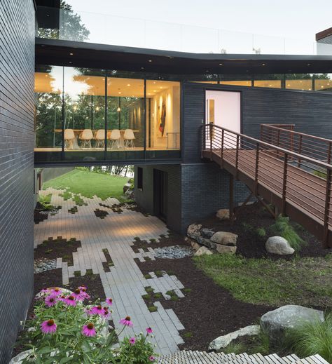 This sculptural home set deeply into the hillside of the Stillwater countryside features charred wood siding (shou sugi ban), cantilevered roof overhangs, and a glass bridge that visually separates the public and private spaces of the house. House Bridge Walkways, Glass Atrium House, House With Bridge Walkway, Bridge To House Entrance, Houses With Bridges, House With Bridge, Bridge Homes, Cantilever Roof, Houses On Slopes