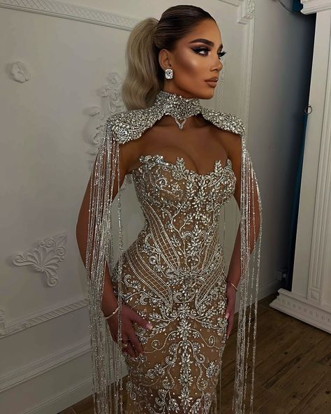 To order this gown, send us a DM at @reineecouture. This couture gown is a masterpiece of opulence and intricate design, perfect for making a grand entrance at any high-profile event. The gown features a form-fitting silhouette that gracefully accentuates the body’s natural curves, exuding both elegance and sophistication. **Bodice and Neckline:** - The bodice showcases a dramatic sweetheart neckline, intricately adorned with shimmering crystals and pearls. - An exquisite high-neck collar a... Nude Gown, Custom Made Dresses, Champagne Evening Dress, Shoulder Cape, Silver Gown, Exquisite Gowns, Embellished Gown, Illusion Dress, Stunning Gowns