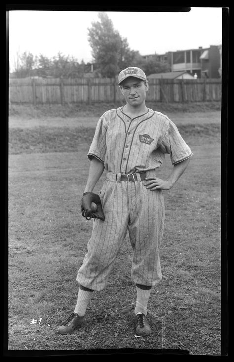 Vertical, black and white photograph of an exterior view depicting a man wearing a baseball uniform and a catcher's mitt on his right hand. He holds a baseball in the mitt, and his other hand is on his hip. There is a field, wooden fence, and houses visible in the distance. Old Baseball Photos, Vintage Baseball Photos, Vintage Baseball Uniforms, Sports Product Photography, 1900s Pictures, Vintage Baseball Aesthetic, 1950s Baseball, Baseball Poses, Baseball Aesthetic