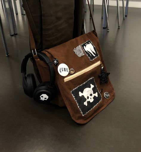 A brown bag with lots of black and white selfmade accessories Alt Schoolbag, Cross Body Bags Aesthetic, Punk Messenger Bag, Diy Fabric Accessories, Bag Patches Aesthetic, Goth Backpack Diy, Cute Cross Body Bags, Pin Bags Ideas, Diy Fabric Bag