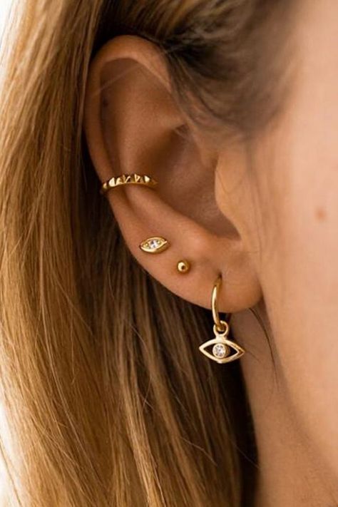 A woman wearing multiple gold evil eye earrings. Cuff Piercings, Gold Ear Piercings, Ušný Piercing, Piercing Face, Ear Cuff Piercing, Ear Piercings Chart, Ear Piercings Tragus, Cool Ear Piercings, Pretty Ear Piercings