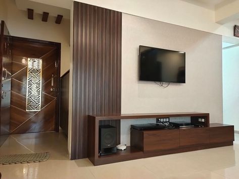 📺 T.V. Unit Wall with Wooden Wall Panelling highlighted with Vertical Grooves, Wooden 📺 TV Cabinet with Drawers & Shelf & View to Entrance Wooden Jali Door highlighted with Grooves and Metal Jali in its Center - GharPedia Tv Unit Near Entrance Door, T V Unit, Wooden Jali Door, Tv Panelling, Office Wall Cabinets, Metal Jali, Wooden Wall Panelling, Wooden Jali, Tv Unit Wall