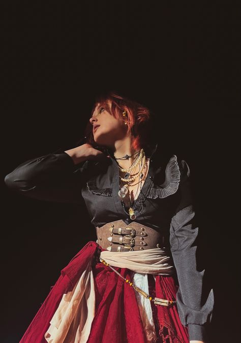 an angle from below of a young woman with red hair against a black sky. she is wearing a frilly black blouse, layered beaded and pearl necklaces, a red skirt with cream lacey under layer, a buckled corset belt, and scarves and sashes around the waist. Pirate Aesthetic Clothing Male, Cool Pirate Outfit, Red Pirate Aesthetic, Fem Pirate, Pirate Core Aesthetic, Black Pirate Costume, Dnd Clothes, Pirate Witch, Pirate Corset