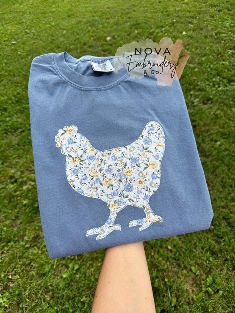 This appliqué Shirt/Sweatshirt has a beautiful floral fabric embroidered on the Tshirt/ Sweatshirt with this cute chicken design. It gives the best farmhouse look, and you can't pass having this up🤍🤍 *SWEATSHIRT option 1. is Gildan brand * adult unisex sizing * 1x1 ribbed collar, cuffs and waistband with spandex * double needle stitching * midweight 8.0 oz. * 50% cotton, 50% polyester * Heather Sport colors are 60% polyester, 40% cotton SWEATSHIRT option 2. is Jerzees brand * adult unisex sizing * tear away label * pill resistant fleece * midweight 8.0 oz. * 50% cotton and 50% polyester * oxford is 49% cotton and 51% polyester *T-SHIRT is comfort colors brand * unisex sizing * relaxed fit * tubular body * twill label * soft-washed garment dyed fabric * 6.1 oz. 100% cotton *please refer t Embroidery Shirt Ideas, Patchwork Shirt Diy, Chicken Applique, Embroidered Chicken, Patchwork Tshirt, Chicken Sweatshirt, Chicken Design, Retro Farmhouse, Chicken Shirt