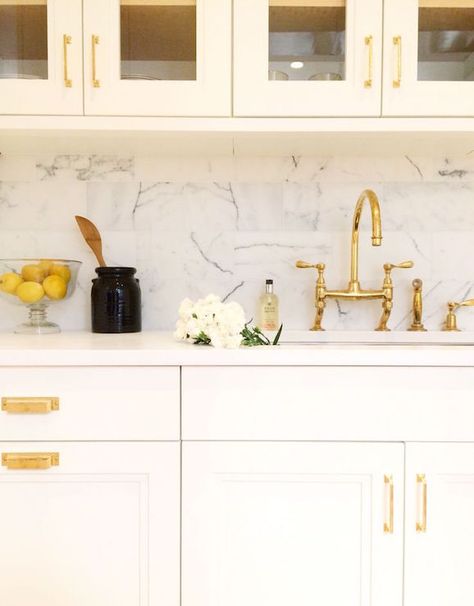 Stunning kitchen features glass-front upper cabinets over ivory lower cabinets accented with gold pulls topped with white marble countertops framing a stainless steel sink and a gold bridge faucet placed in front of a marble staggered backsplash. Gold Kitchen Hardware, Kitchen With Marble, Glam Kitchen, Modern Kitchen Sinks, Gold Faucet, Kitchen Sink Design, Kitchen Design Color, Apartment Decoration, Marble Backsplash