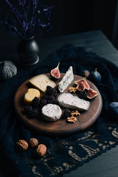 Dark-stained wooden cheese board with an assortment of cheeses, blackberries, figs, and walnuts, set on a black lace cloth with dim lighting and gothic decor. Cheese Board Aesthetic, Cheese Board Ideas, Board Aesthetic, Wooden Cheese Board, Board Ideas, Dining Experiences, Cheese Board, Cheese