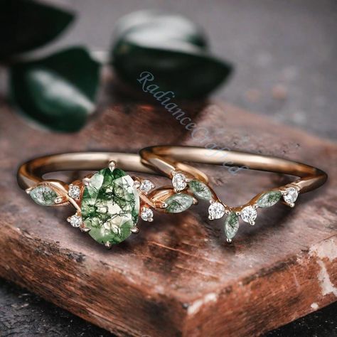 This vintage-inspired engagement ring features an oval-cut green moss agate at its center, radiating a unique and earthy charm. The ring is crafted in elegant rose gold and designed in an art deco style, which gives it a timeless and sophisticated look. Surrounding the moss agate are delicate cluster accents that resemble leaves, adding a nature-inspired touch to the design. This bridal set is perfect for women who appreciate a blend of classic elegance and natural beauty, making it an ideal cho Vintage Green Engagement Ring, Moss Agate Wedding Ring Set, Earthy Engagement Rings, Earthy Wedding Rings, Green Wedding Rings, Creative Engagement Rings, Agate Wedding Ring, Art Deco Rose, Agate Wedding