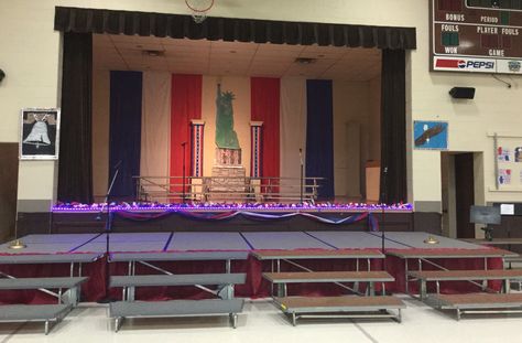 Red, white and blue backdrop created with plastic tablecloth rolls; they were attached under the lay in ceiling and hung vertically in strips. What you see is the actual width of the tablecloth. Columns belong to the school, and were decorated with patriotic bunting from Oriental Trading. See separate post about the Statue of Liberty and the lighted garland across the stage. Patriotic Backdrop Ideas, Red White And Blue Backdrop, Kindergarten Graduation Themes, Musical Decor, Patriotic Activities, Lighted Garland, Veterans Day Activities, Patriotic Bunting, Patriotic Food