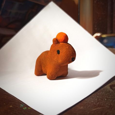 Capybara with orange on its head Cute Clay Capybara, Gort Capybara, Capybara Clay Sculpture, Cute Mini Sculptures, Easy Sculpey Clay Ideas, Air Dry Clay Capybara, Cute Mini Clay Sculptures, Polymer Clay Capybara, Capybara Clay Art