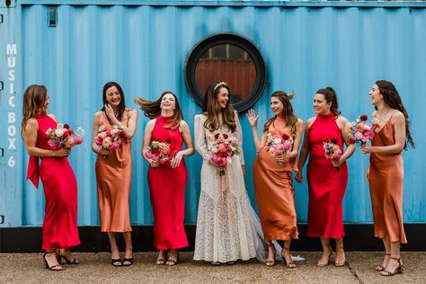 Bridesmaids in v-neck satin burnt orange dresses or bright red high neck dresses with bride in lace wedding dress and headband all holding matching pink and red wedding bouquets Red Satin Dresses, Wedding Dress With Bridesmaids, Orange Wedding Color Scheme, Burnt Orange Dresses, Sunset Wedding Theme, Orange Wedding Color Palette, Rixo Dress, Orange Dress Wedding, Orange Wedding Bouquet