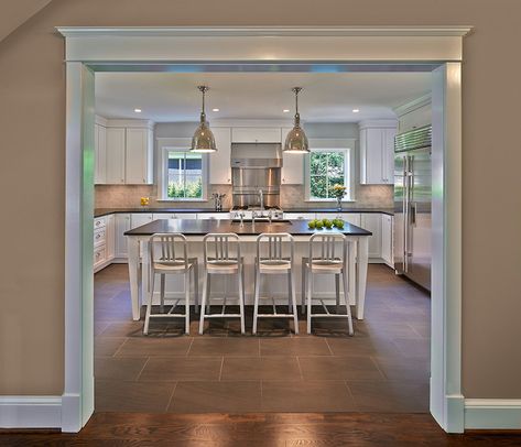 U shaped kitchen features Restoration Hardware Benson Pendants illuminating a white island with legs topped with honed black countertops framing sink lined with Emeco 1006 Navy Counter Stools atop gray tiled floor laid out in brick pattern. Kitchen Island In Front Of Doorway, Kitchen Island With Pillar In Middle, Kitchen With Columns Islands, Kitchen Island With Columns In Middle, Structural Post In Kitchen Island, Structural Beam In Kitchen Island, Grey Tile Kitchen Floor, Grey Kitchen Tiles, Kitchen Restoration