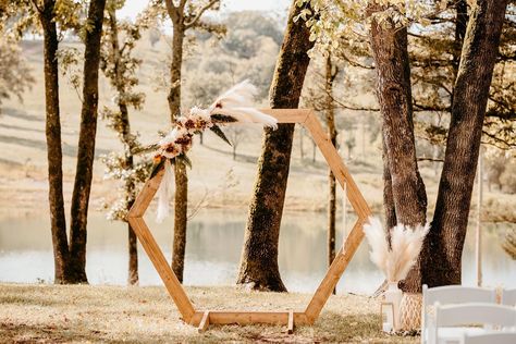 Outdoor wedding ceremony, wooden octagon shaped backdrop/arbor, muted peach color palette, pampas grass, desert color palate, setting in the tress with the sun setting and water behind the arbor. Wedding Hexagon Arch, Wedding Hexagon, Hexagon Backdrop, Hexagon Wedding Arch, Wedding Canopy Outdoor, Simple Wedding Arch, Hexagon Arch, Rustic Pink Wedding, Pew Decor