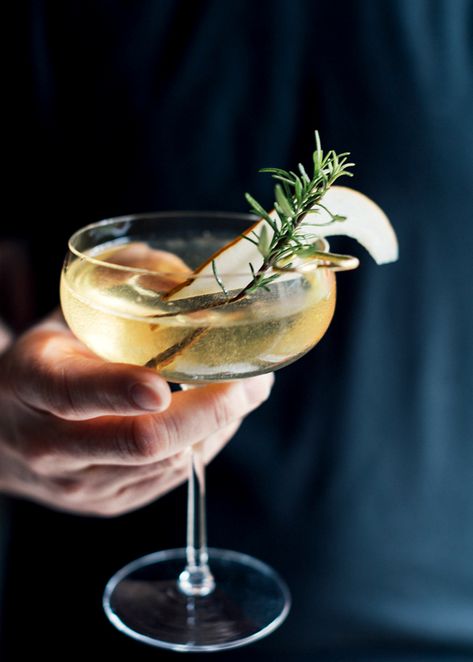 A hand grasping a modern coupe glass filled with a golden liquid is set against a dark black cloth, probably the shirt of the person holding the drink. A slice of pear and sprig of rosemary garnish the drink. Pear Syrup Recipe, Pear Simple Syrup, Pear Syrup, Elderflower Champagne, Late Autumn, Rosemary Sprigs, Champagne Cocktail, Syrup Recipe, Cocktail Glass