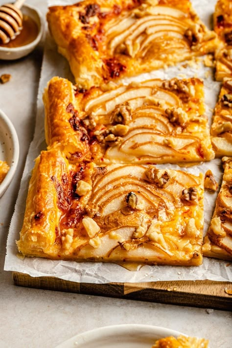 Gorgeous pear puff pastry tart with spicy cheddar cheese, toasted walnuts, and a drizzle of honey. This delicious, easy pear tart recipe makes the perfect appetizer for impressing friends & family and takes just 15 minutes to prepare! Serve warm or at room temp and watch guests devour. #appetizer #pears #puffpastry #newyearseve #holiday Persimmon Puff Pastry, Pear Puff Pastry, Holiday Tarts, Pear Tart Recipe, Ambitious Kitchen Recipes, Pear Desserts, Savoury Bites, Phyllo Dough Recipes, Entertaining Appetizers